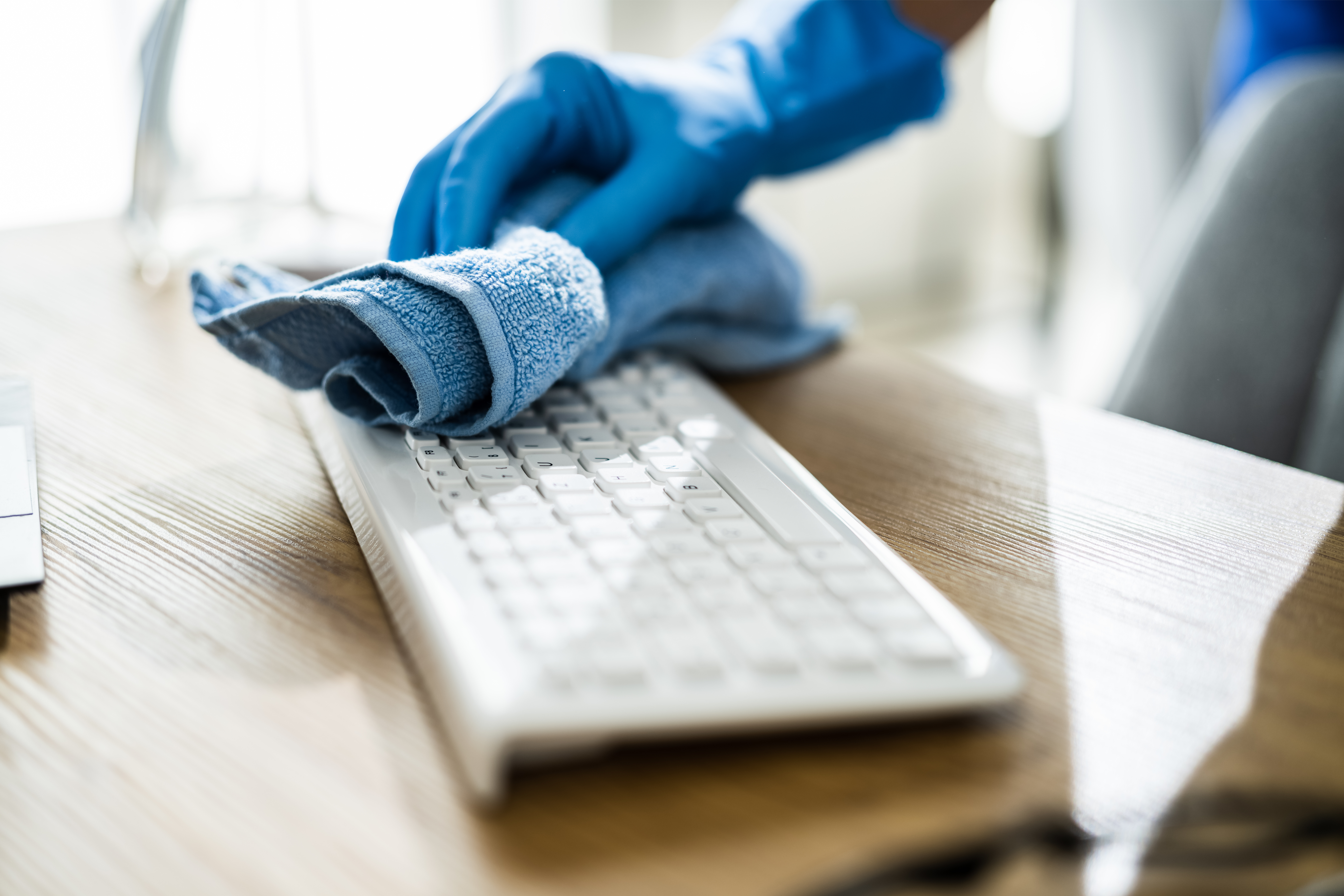 a cleaner using a blue cloth to clean a computer keyboard to show the best cleaning practices for your office following covid-19