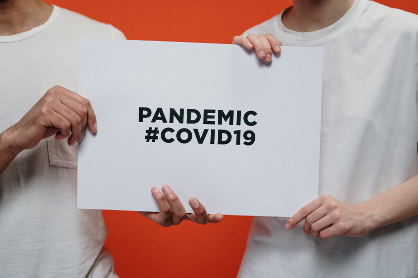 Two people holding a sign saying pandemic covid 19 representing how covid has affected temporary staff recruitment agencies