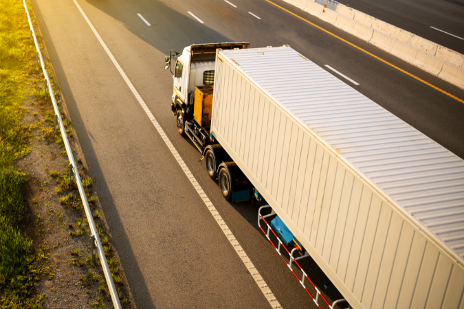 A skilled logistics driver driving a white lorry confidently down a long road who has been hired for their indispensable qualities.