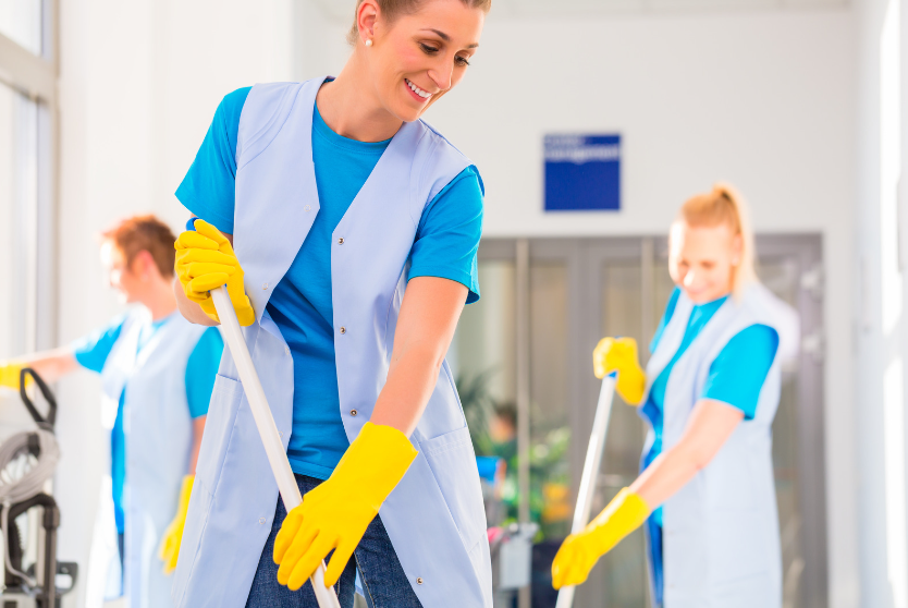 three women wearing blue cleaning uniform and yellow gloves mopping a public walkway to show why retail businesses should use a commercial cleaning service provider